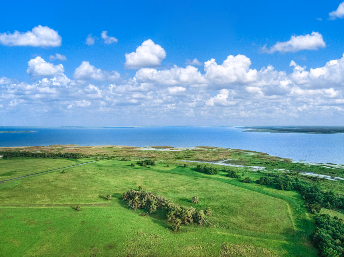Open green land beside a lake under a cloudy sky.